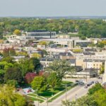 Aerial view of downtown Waukesha, Wisconsin, showcasing residential neighborhoods, historic buildings, and a prominent church steeple surrounded by lush green trees.