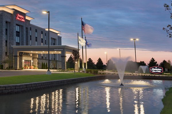 Exterior view of Hampton Inn & Suites Kenosha with a lit water fountain and flags at sunset.
