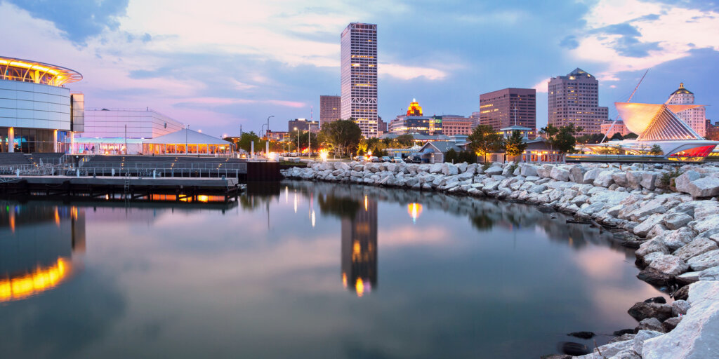Downtown Milwaukee skyline at dusk reflecting in Lake Michigan, featuring modern buildings and the Milwaukee Art Museum.