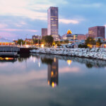 Downtown Milwaukee skyline at dusk reflecting in Lake Michigan, featuring modern buildings and the Milwaukee Art Museum.