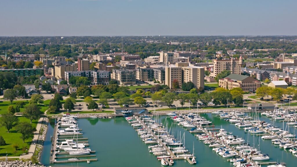 Aerial view of Kenosha, Wisconsin, showcasing downtown buildings and a marina filled with boats along Lake Michigan.