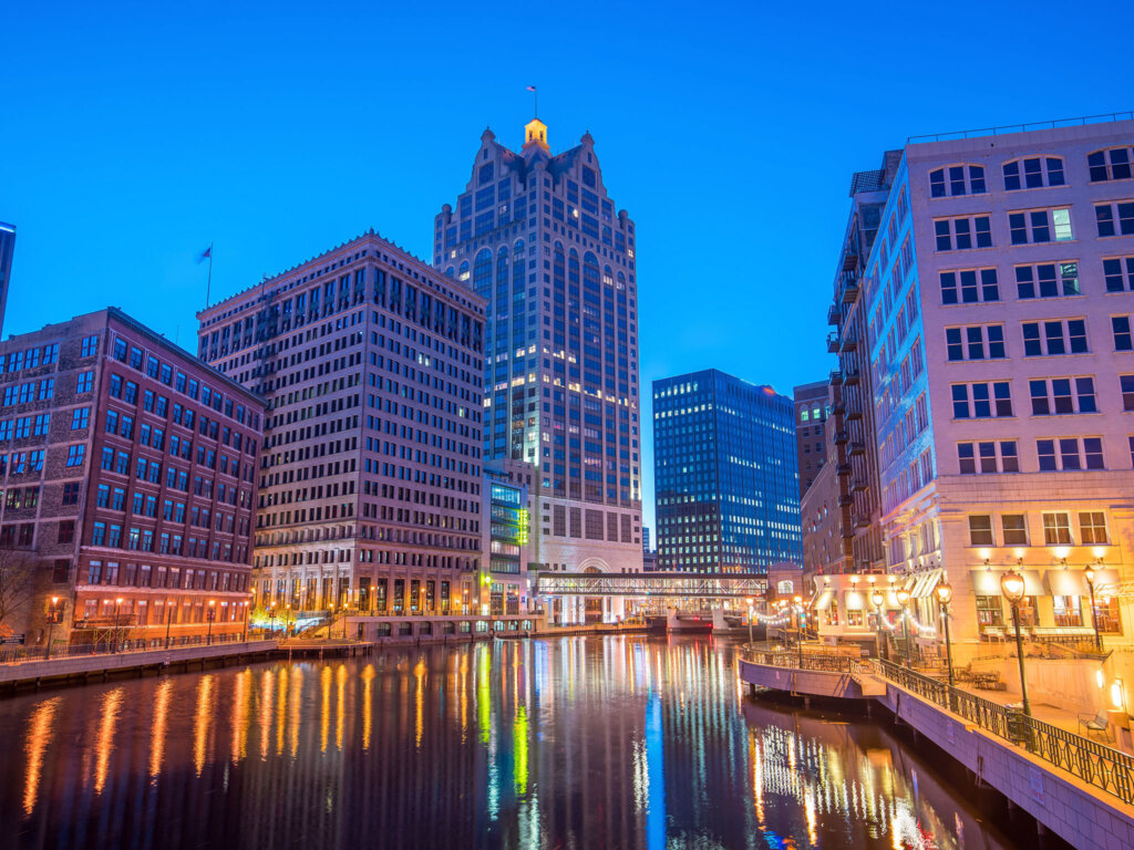 Downtown Milwaukee skyline at dusk with city lights reflecting on the Milwaukee River.
