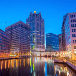 Downtown Milwaukee skyline at dusk with city lights reflecting on the Milwaukee River.