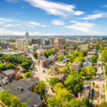 Aerial view of downtown Madison, Wisconsin, featuring the State Capitol building and tree-lined streets on a bright, sunny day.