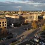 Aerial view of downtown Kenosha, Wisconsin, featuring historic buildings, autumn trees, and Lake Michigan in the background under a partly cloudy sky.