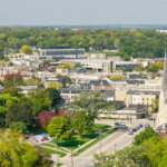 Aerial view of downtown Waukesha, Wisconsin, showcasing historic buildings, a church, and tree-lined streets during spring.