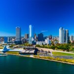A vibrant aerial view of downtown Milwaukee’s skyline along Lake Michigan, featuring modern high-rise buildings, the Milwaukee Art Museum, and clear blue skies.