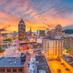 Downtown Milwaukee skyline at sunset with colorful buildings and glowing city lights.