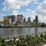 Scenic view of downtown Milwaukee skyline with modern and historic buildings along the river under a partly cloudy sky.