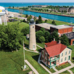 Aerial view of the Southport Lighthouse and historic buildings in Kenosha, Wisconsin, with Lake Michigan and a water tower in the background.
