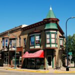 Historic brick building with green and red trim on a sunny street corner in downtown New Berlin.