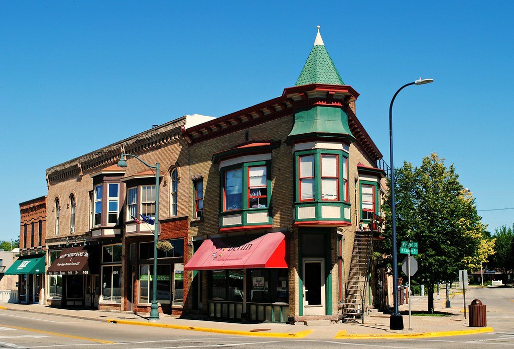 Historic brick building with green and red trim on a sunny street corner in downtown New Berlin.