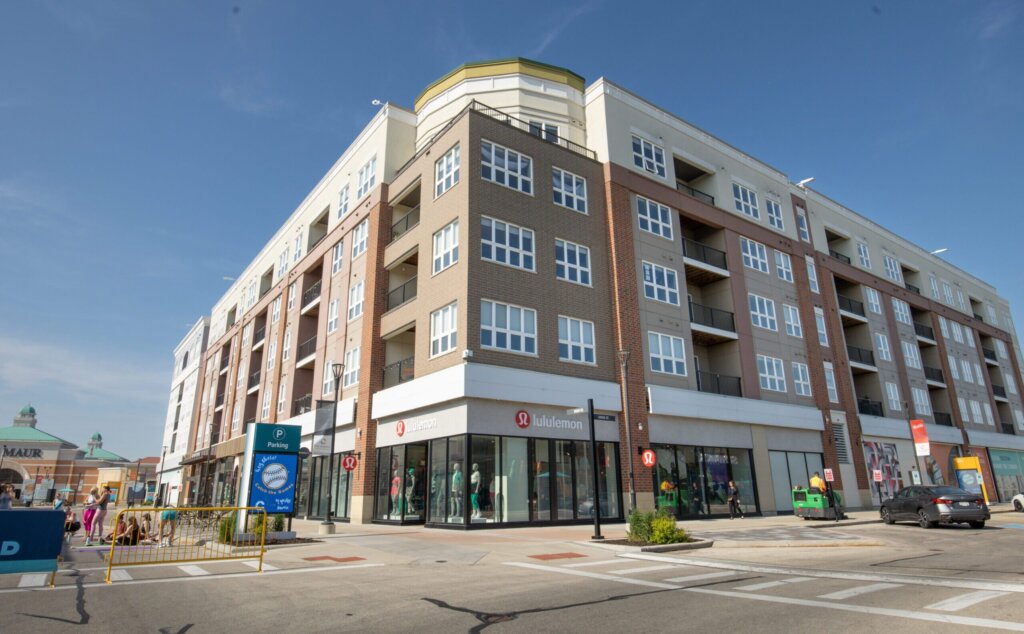 Modern mixed-use apartment building in Brookfield with retail stores at street level, including Lululemon, under a clear blue sky.