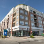 Modern mixed-use apartment building in Brookfield with retail stores at street level, including Lululemon, under a clear blue sky.