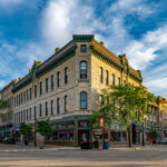 Historic corner building in downtown Wauwatosa, Wisconsin, under a vibrant blue sky with tree-lined streets and local shops.