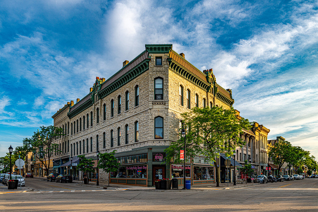 Historic corner building in downtown Wauwatosa, Wisconsin, under a vibrant blue sky with tree-lined streets and local shops.