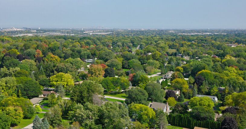 Aerial view of a suburban neighborhood in Brookfield, Wisconsin, surrounded by dense green trees under a clear sky.