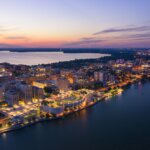 Aerial view of downtown Madison, Wisconsin at dusk, featuring the Capitol building, lit city streets, and Lake Monona shoreline.