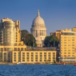Skyline view of downtown Madison, Wisconsin with the State Capitol building centered behind modern waterfront buildings along Lake Mendota.