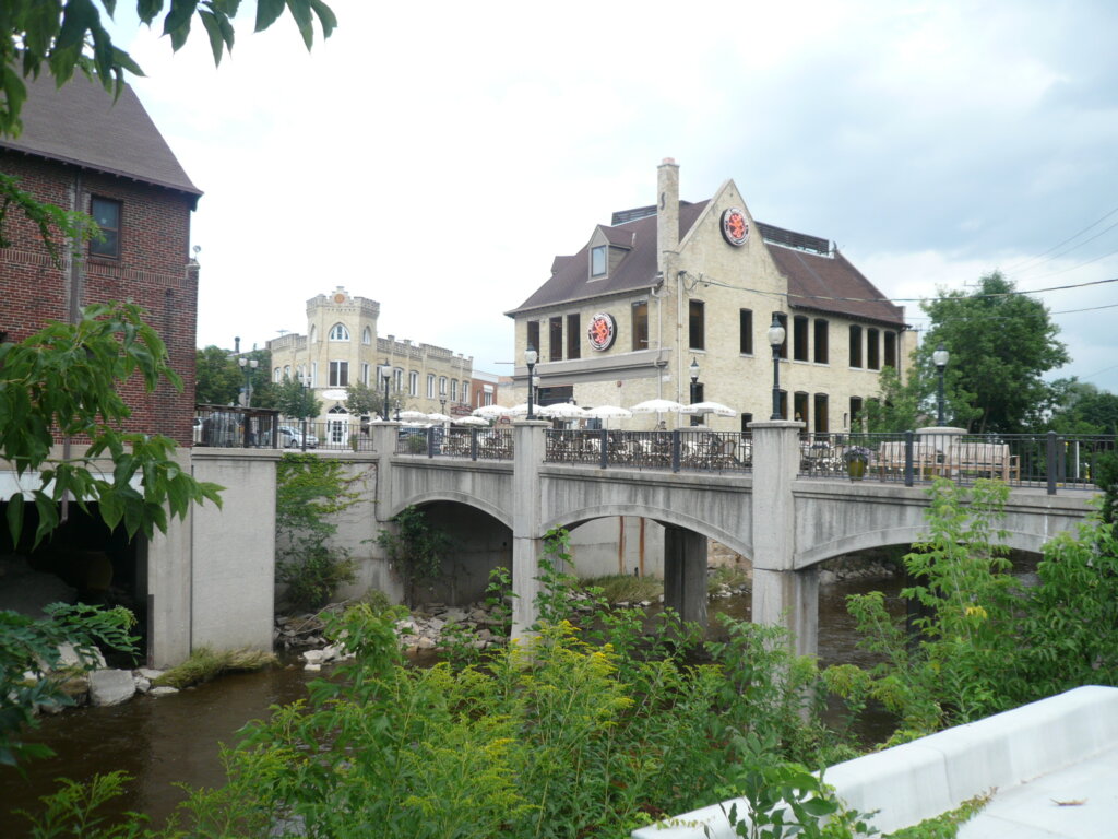 Bridge over a small river in downtown Wauwatosa, Wisconsin, with historic buildings and outdoor restaurant seating in view.