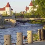 Scenic riverwalk in downtown Waukesha with stone bridge, flowing river, and historic buildings in the background.
