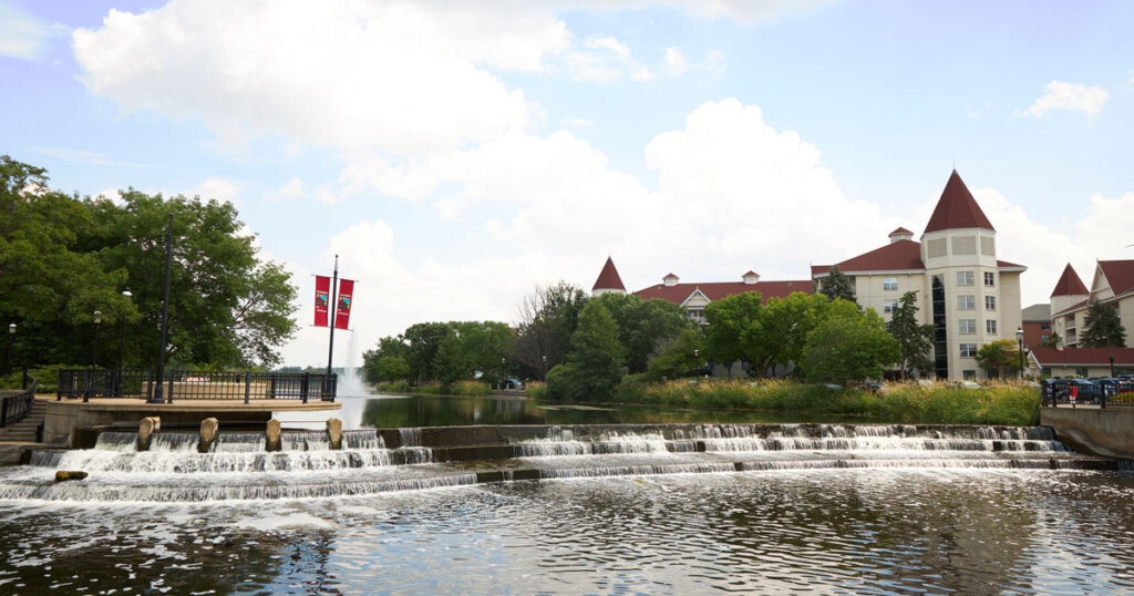 Scenic view of a stepped waterfall and historic-style buildings in downtown Waukesha, Wisconsin, under a partly cloudy sky.