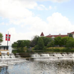 Scenic view of a stepped waterfall and historic-style buildings in downtown Waukesha, Wisconsin, under a partly cloudy sky.