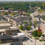 Aerial view of a small downtown area with historic buildings, tree-lined streets, and surrounding greenery.