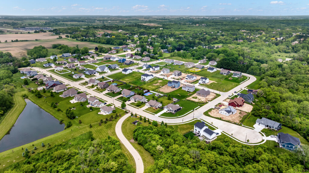 Aerial view of a suburban neighborhood in Kenosha, Wisconsin, featuring newly built homes, green lawns, and surrounding wooded areas.