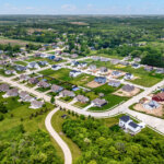 Aerial view of a suburban neighborhood in Kenosha, Wisconsin, featuring newly built homes, green lawns, and surrounding wooded areas.