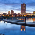 Milwaukee skyline at dusk reflected in calm waters with a dock in the foreground.