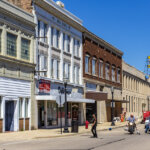 Historic downtown street view in Kenosha, Wisconsin featuring vintage brick buildings, local businesses, and motorcycles on a sunny day — a visual representation of the vibrant community where homeowners often seek opportunities to sell in Kenosha, even if their properties need repairs.
