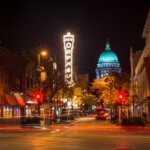 Downtown Madison at night with the Wisconsin State Capitol dome glowing in the background and the Orpheum Theatre sign lit up.