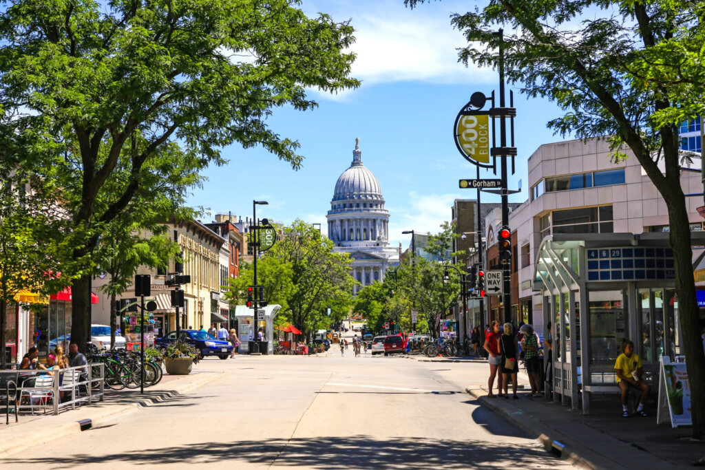 Street view in downtown Madison with the Wisconsin State Capitol in the background on a sunny day.
