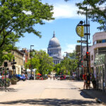 Street view in downtown Madison with the Wisconsin State Capitol in the background on a sunny day.