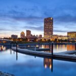 Milwaukee city skyline at dusk with reflections on the river and a modern dock in the foreground.