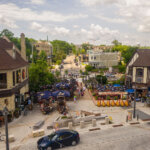 A lively outdoor beer garden in Wauwatosa's Village district, surrounded by people dining under umbrellas, historic buildings, and a charming pedestrian street.
