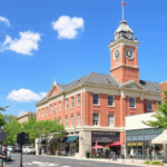 Vibrant downtown Waukesha street with historic red-brick buildings, a clock tower, outdoor cafes, and a bright blue sky.