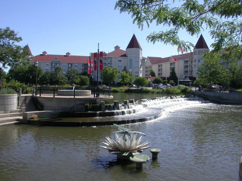 Scenic riverwalk in Waukesha, Wisconsin, with cascading water feature and historic buildings in the background.