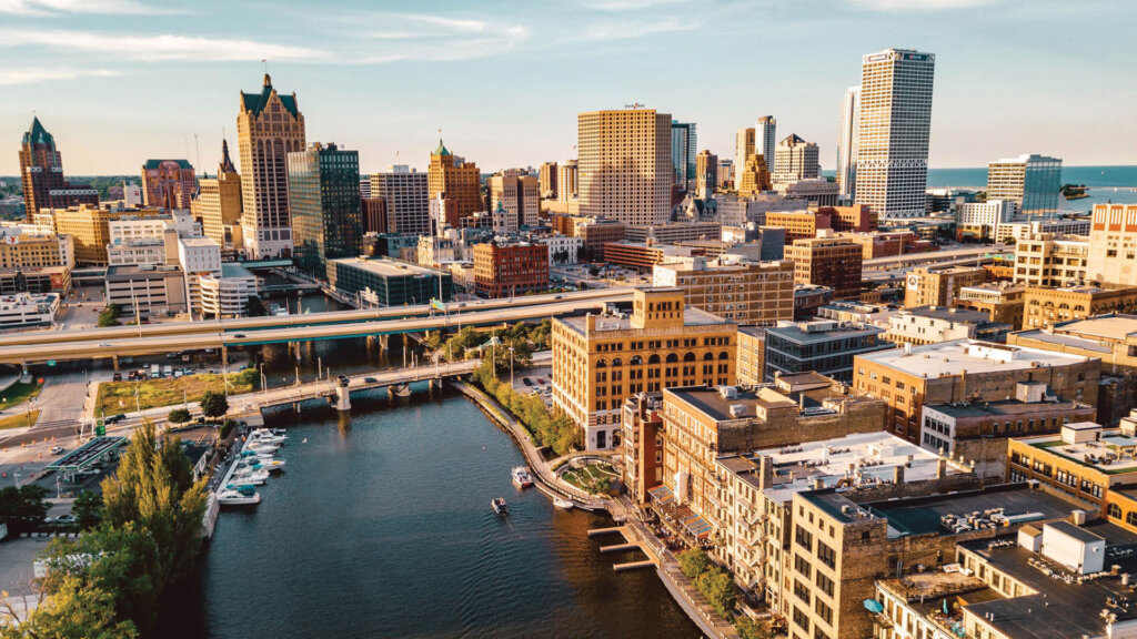 Aerial view of downtown Milwaukee showing modern skyscrapers, historic brick buildings, and the Milwaukee River under a clear blue sky.