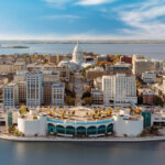 Aerial view of downtown Madison, Wisconsin, featuring the Wisconsin State Capitol and surrounding buildings along the waterfront under a bright blue sky.