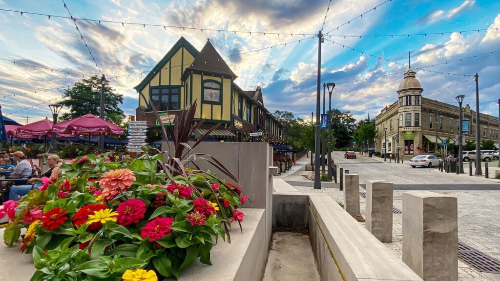 Colorful flowers in the Wauwatosa Village square with historic buildings, outdoor dining, and a dramatic evening sky.