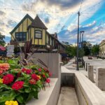 Colorful flowers in the Wauwatosa Village square with historic buildings, outdoor dining, and a dramatic evening sky.