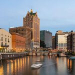 Downtown Milwaukee skyline at dusk with buildings reflecting on the Milwaukee River.