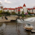 Scenic view of downtown Waukesha with a small waterfall, pond, and red-roofed buildings in the background on a cloudy day.