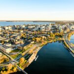 Aerial view of downtown Madison, Wisconsin, showcasing lakeside roads, waterfront parks, and city buildings under clear golden sunlight.