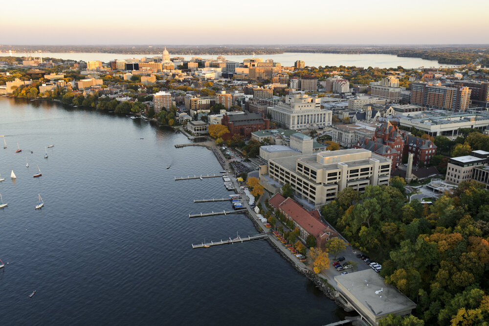Aerial view of downtown Madison, Wisconsin at sunset showing Lake Mendota, sailboats, and the Wisconsin State Capitol in the background.