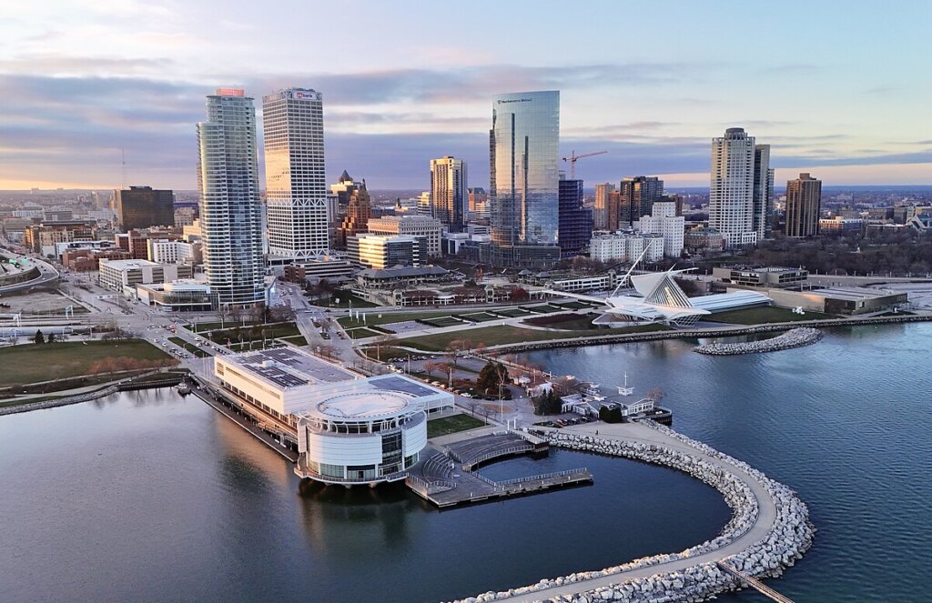 Aerial view of downtown Milwaukee at sunrise, showing modern skyscrapers, the Milwaukee Art Museum, and Lake Michigan’s waterfront.
