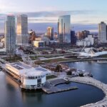 Aerial view of downtown Milwaukee at sunset, showing modern skyscrapers, Lake Michigan shoreline, and the Milwaukee Art Museum’s white winged architecture.