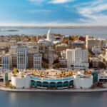 Aerial view of downtown Madison, Wisconsin featuring the Wisconsin State Capitol and surrounding buildings by the lakeshore under a bright blue sky.